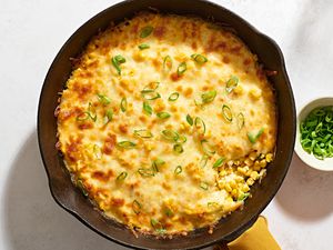 A large skillet of Korean corn cheese, topped with sliced green onions