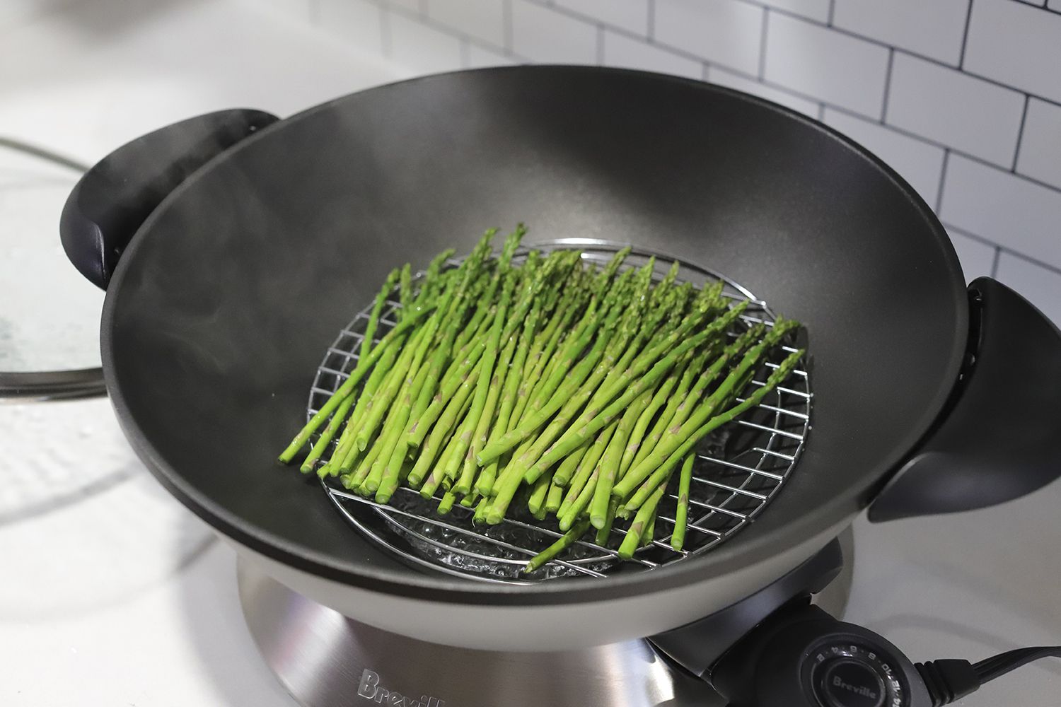 A Breville Hot Wok Pro displayed on a countertop with asparagus in it