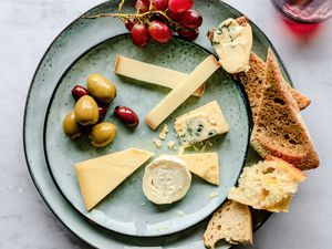 variety of cheeses with bread and olives on a plate