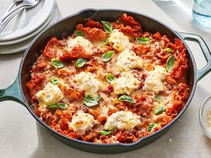 A cast iron pan with skillet lasagna, topped with basil leaves and served with extra Parmesan cheese