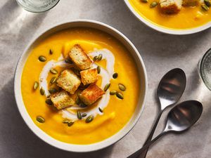 Two bowls of roasted butternut squash soup topped with pepitas, croutons, and sour cream