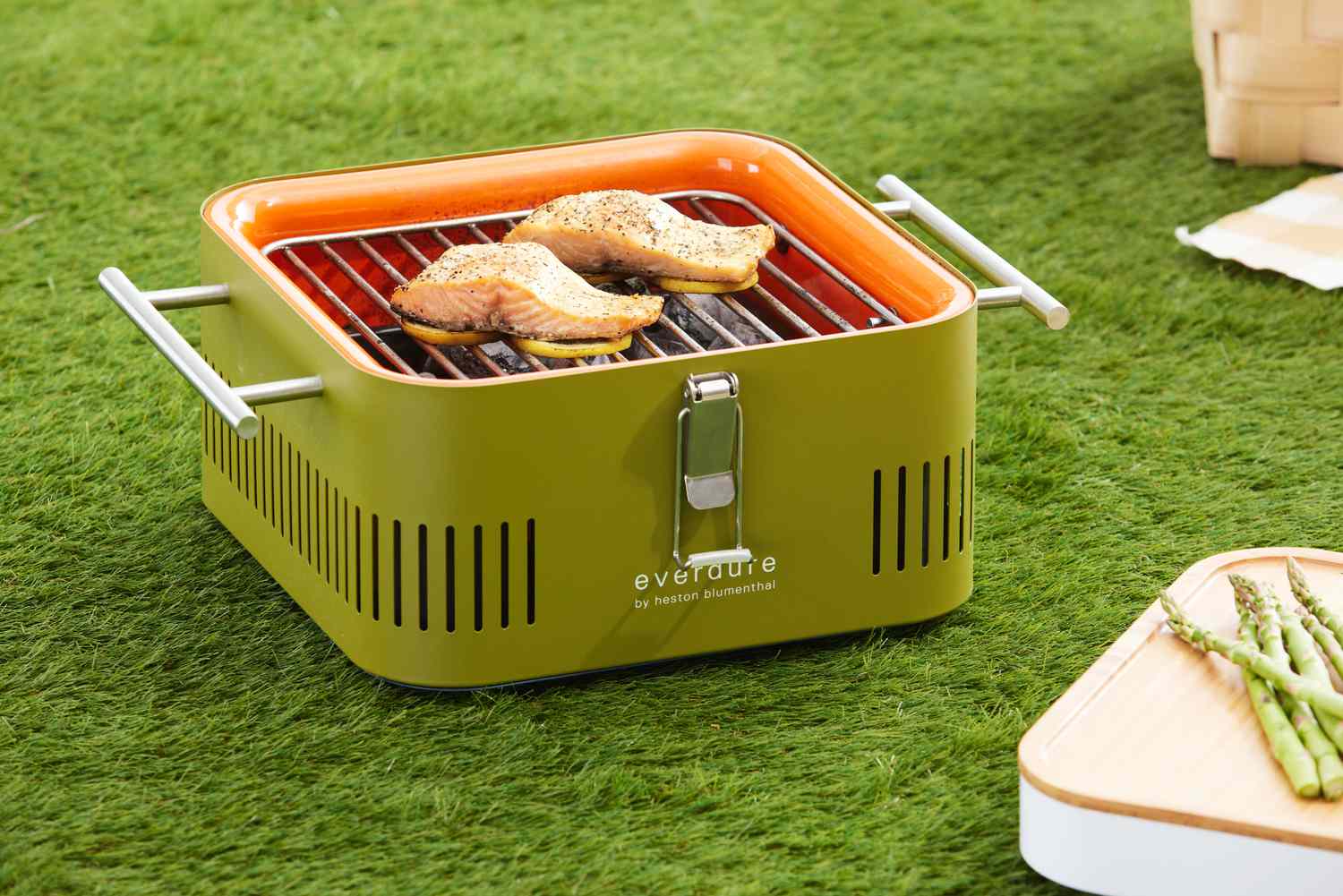 Salmon fillets grilling on lemon slices on Everdure Cube Portable Charcoal Grill displayed on grass 