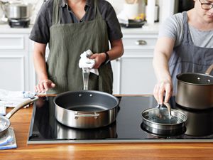 Two people standing in front of nonstick cookware on a glass stovetop in a kitchen