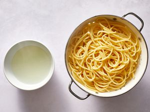 cooked pasta drained in colander with reserved pasta water in bowl