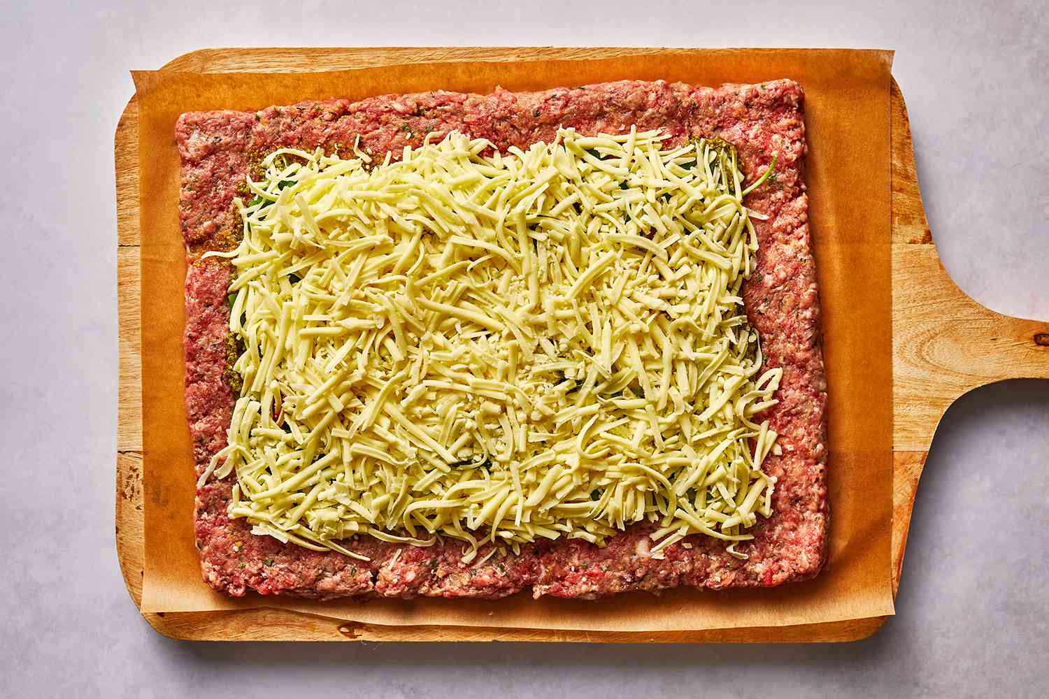 Meat mixture with basil, peppers and cheese on top on a parchment paper lined cutting board 