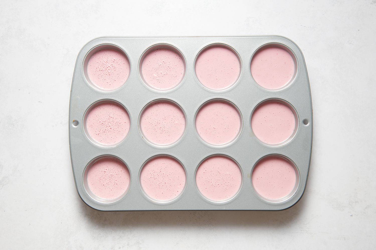 A sprayed muffin pan with filled with strawberry miso mochi muffin batter