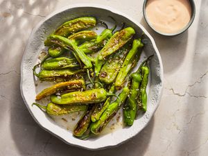 A large bowl of blistered shishito peppers served with a dipping sauce