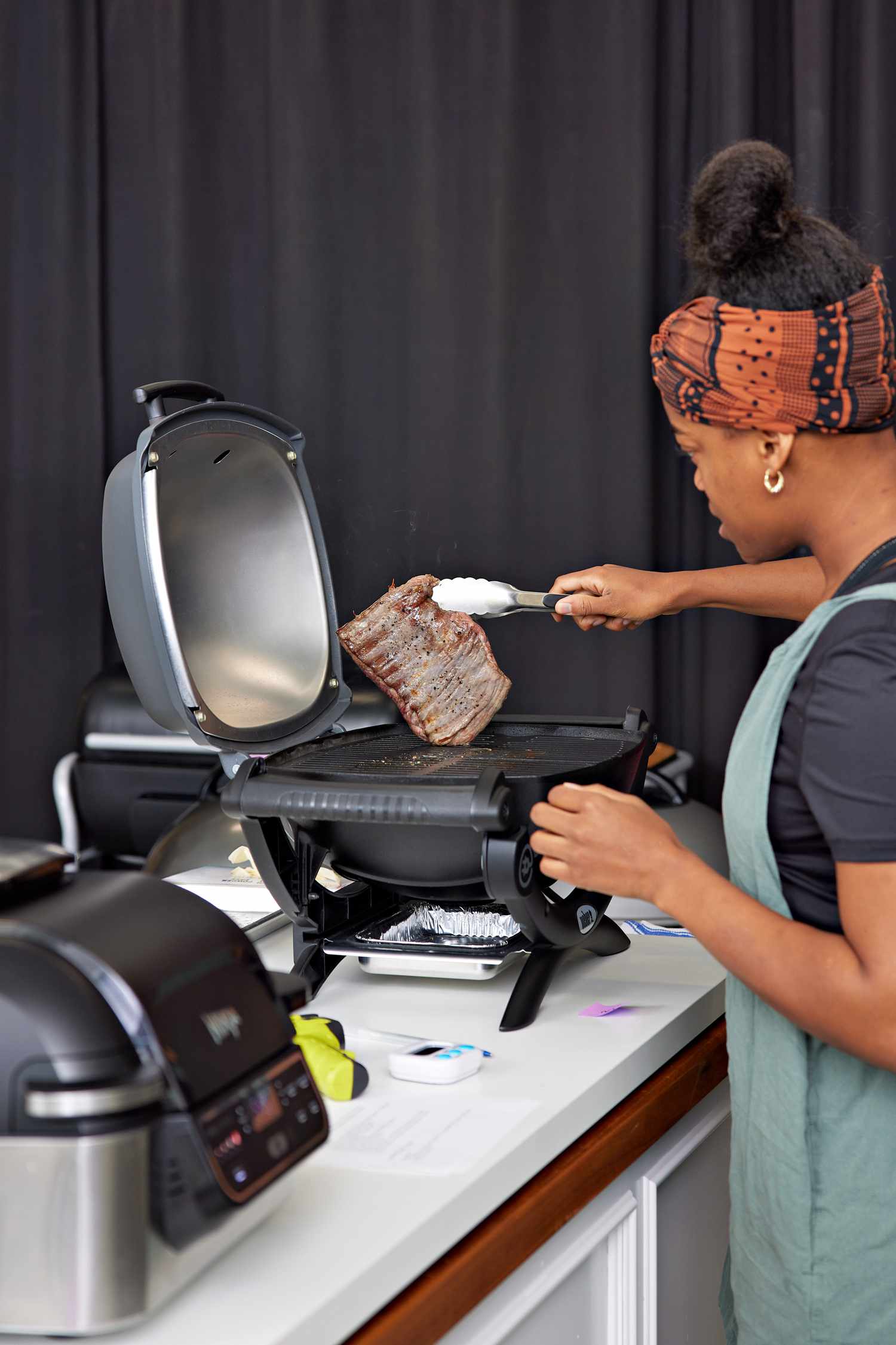 Woman using tongs to flip a steak on a Weber Q 1400 Electric Grill