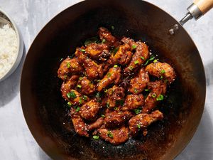 A wok of three cup chicken garnished with sesame seeds and scallions, served with a side of white rice