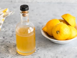 Lemon simple syrup in a bottle next to a bowl of lemons