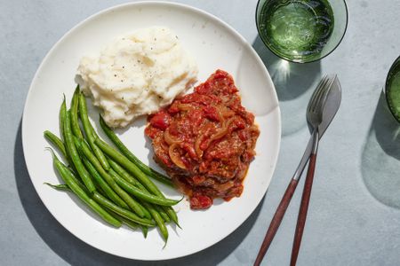 A plate of Swiss steak served with steamed green beans, mashed potatoes, and sparkling water