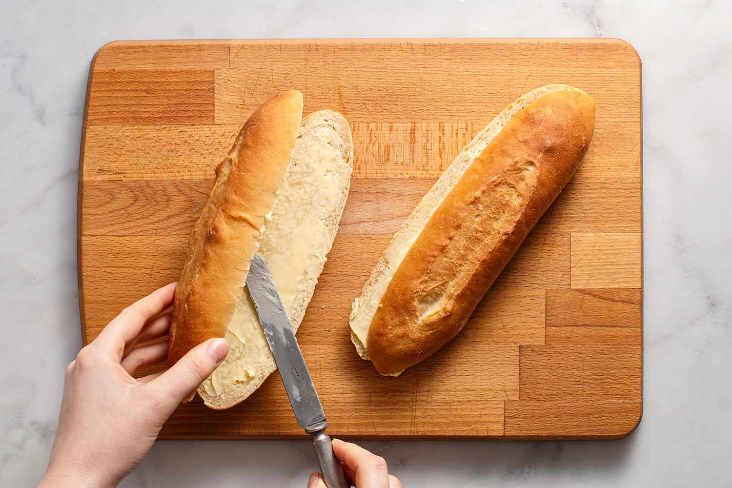 A knife buttering two cut sandwich rolls