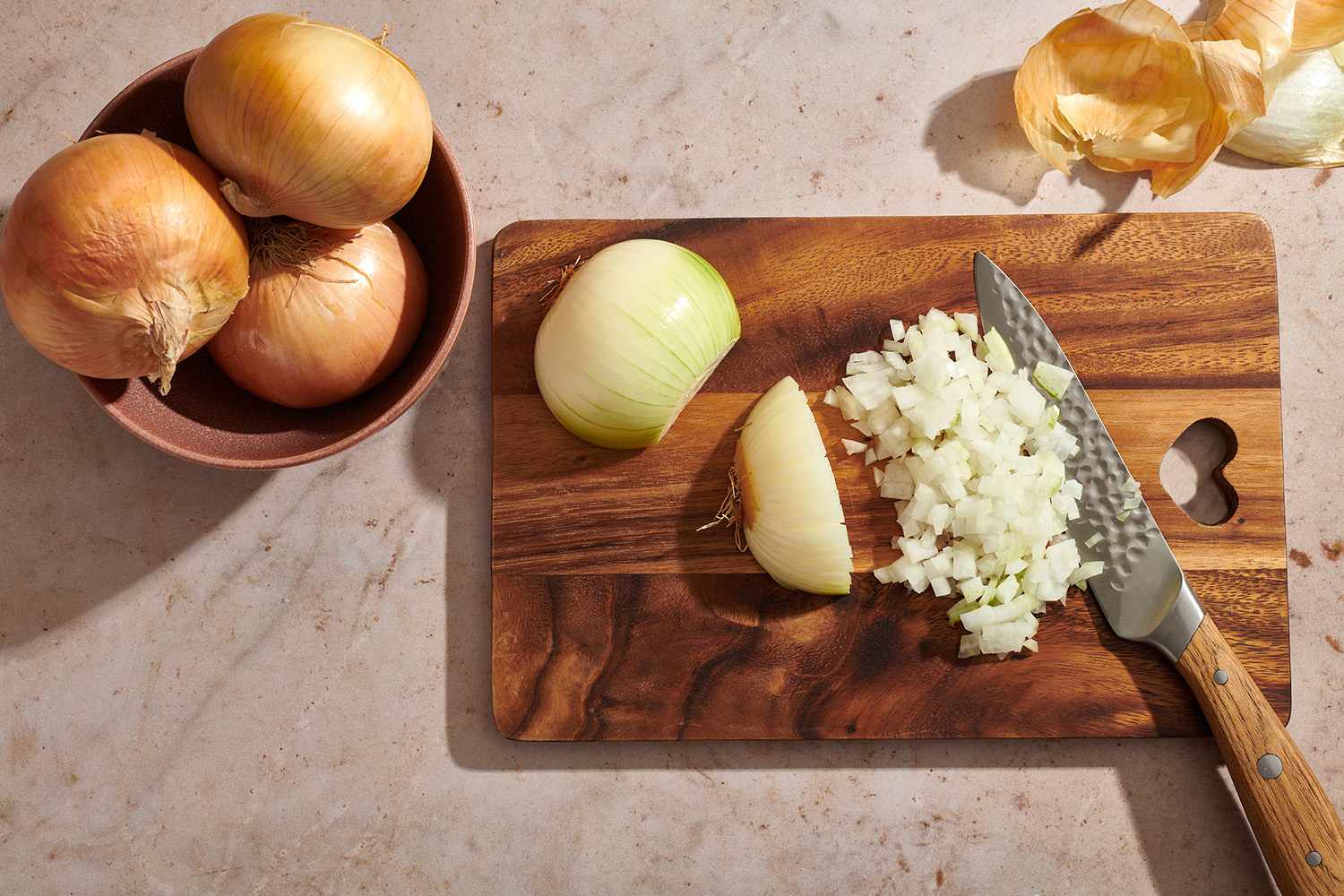 peeled onion on a cutting board partly diced, with chef's knife