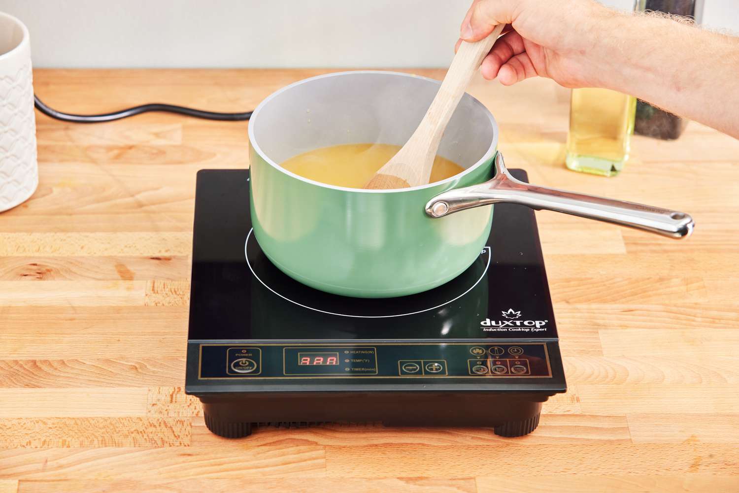 Hand stirring melted butter with wooden spoon in Caraway Cookware Set saucepan on hot plate