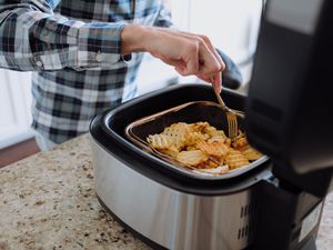 person cooking waffle fries in air fryer