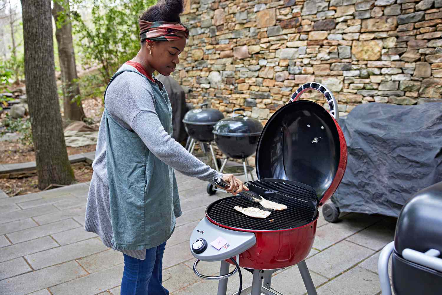 Woman cooking chicken on a red Char-Broil Patio Bistro TRU-Infrared Electric Grill outside