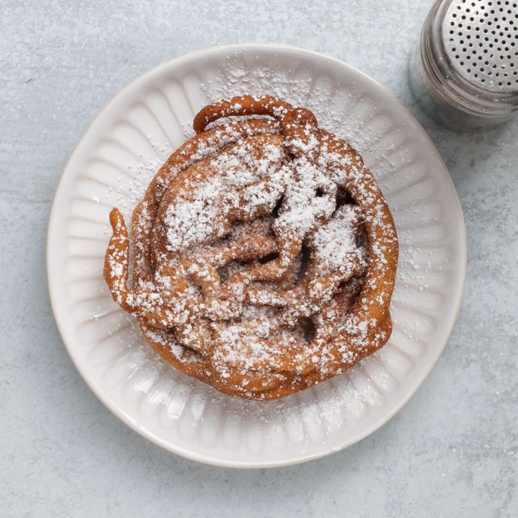 Pancake mix funnel cake on a white plate with a shaker filled with confectioners' sugar nearby