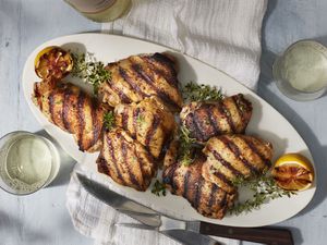 Grilled chicken thighs on an oval plate with sprigs of fresh thyme
