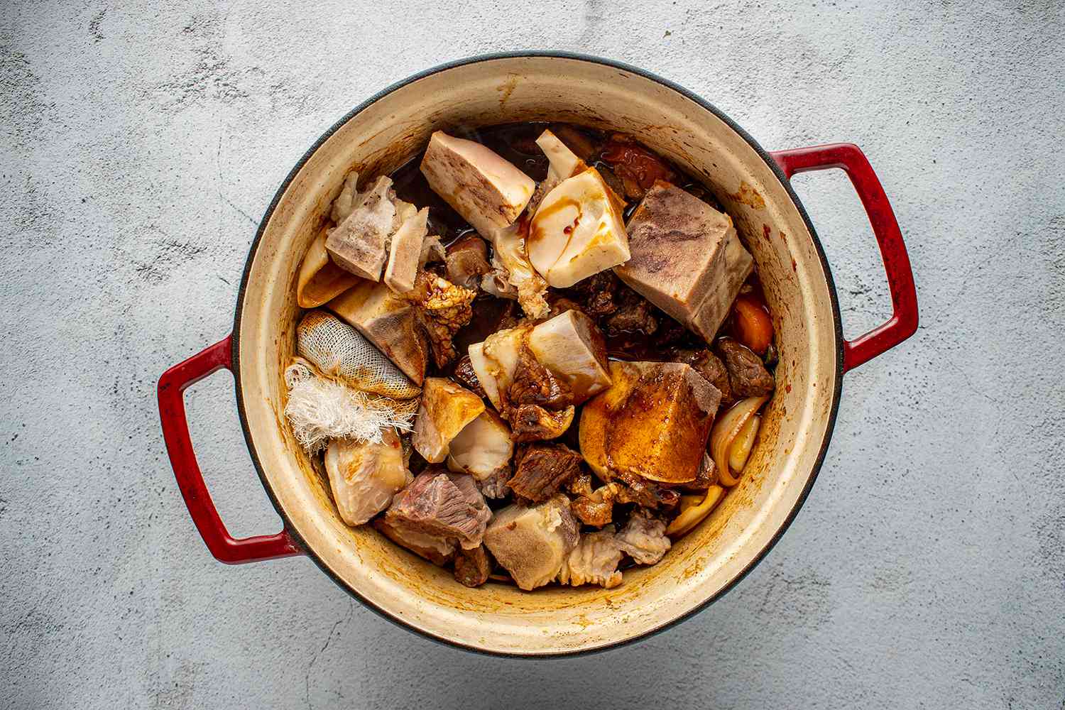 Soy sauce, dark soy sauce, spice sachet, browned beef cubes, and beef bones in a pot