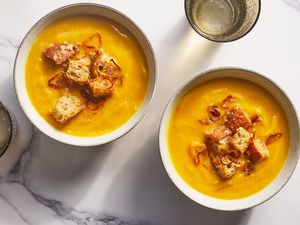 Two bowls of acorn squash soup topped with fried shallots and croutons
