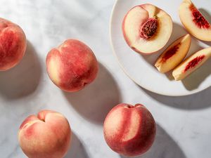 Four peaches on a marble surface, with a halved peach and peach slices on a small plate