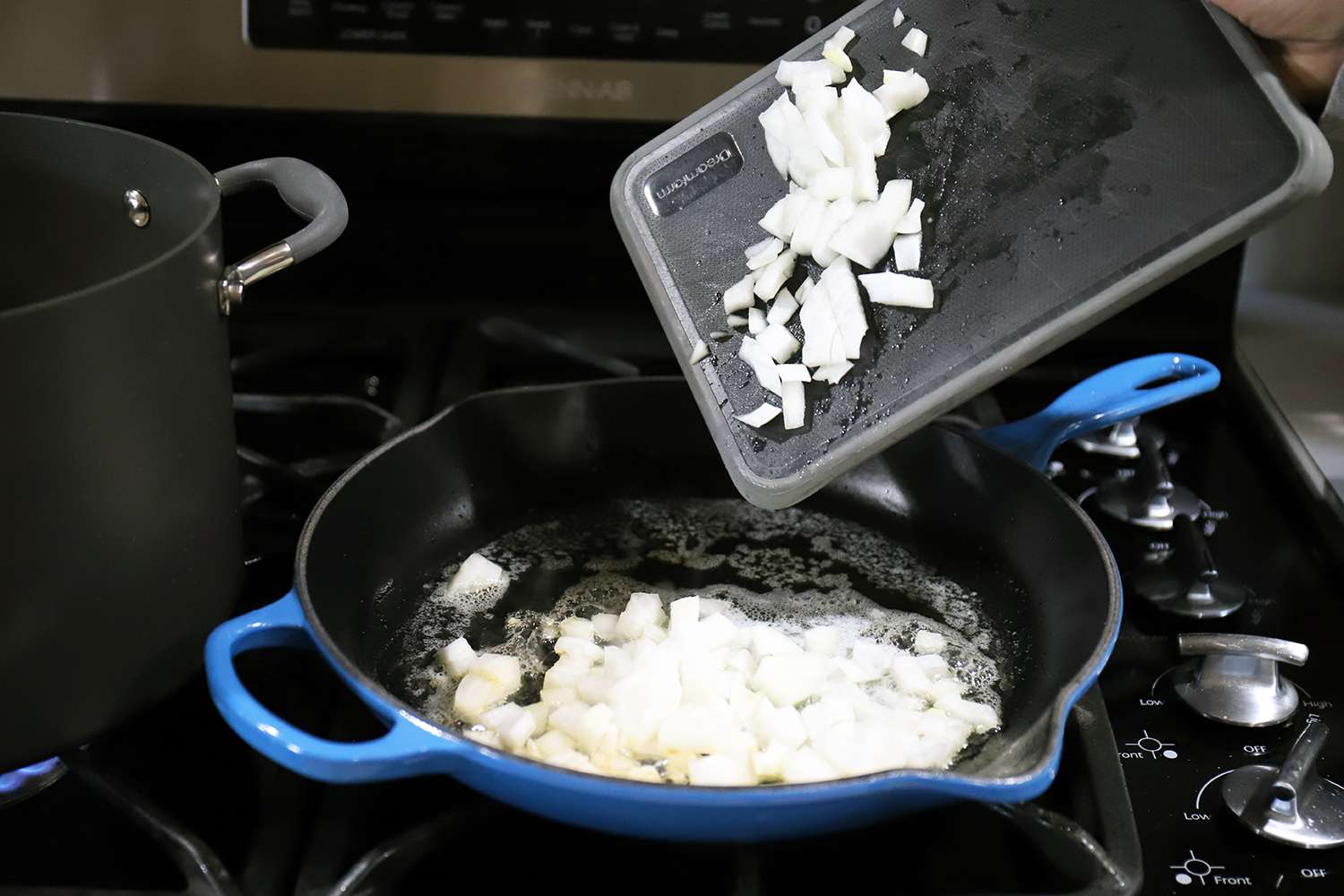 Onions being pushed from a cutting board into the Le Creuset Signature Skillet