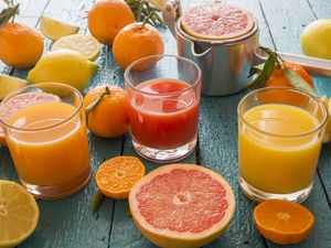 Glasses of orange juice, grapefruit juice and multivitamine juice, juice squeezer and fruits on wood