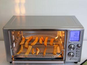 Emeril Lagasse Power AirFryer 360 displayed on a tiled surface with a baking sheet full of French fries inside of it 