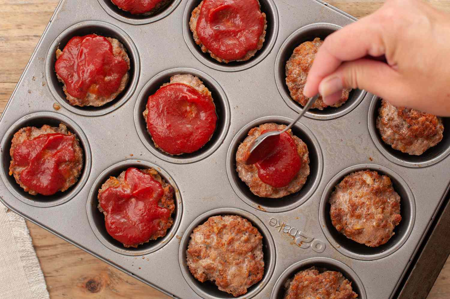 Meatloaf muffins topped with ketchup in a muffin pan before baking