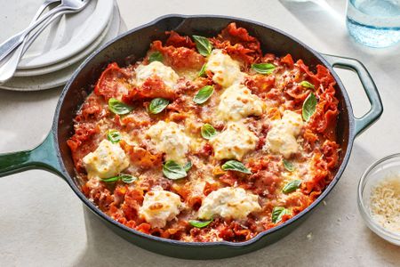 A cast iron pan with skillet lasagna, topped with basil leaves and served with extra Parmesan cheese