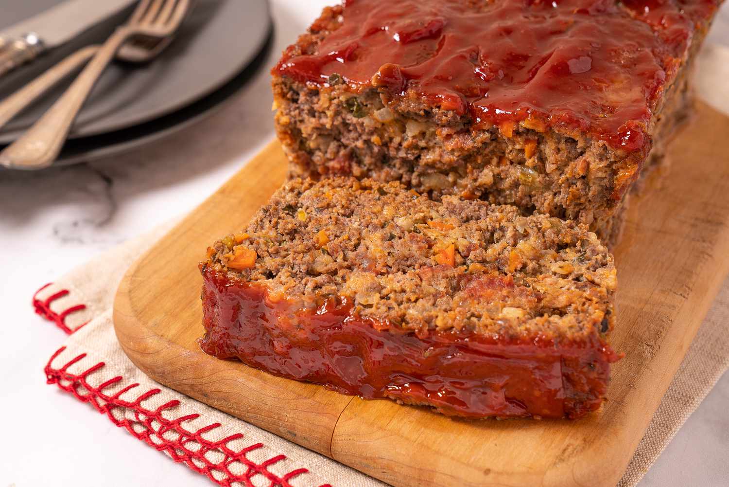 Sliced meatloaf with shiny ketchup glaze on a wooden board
