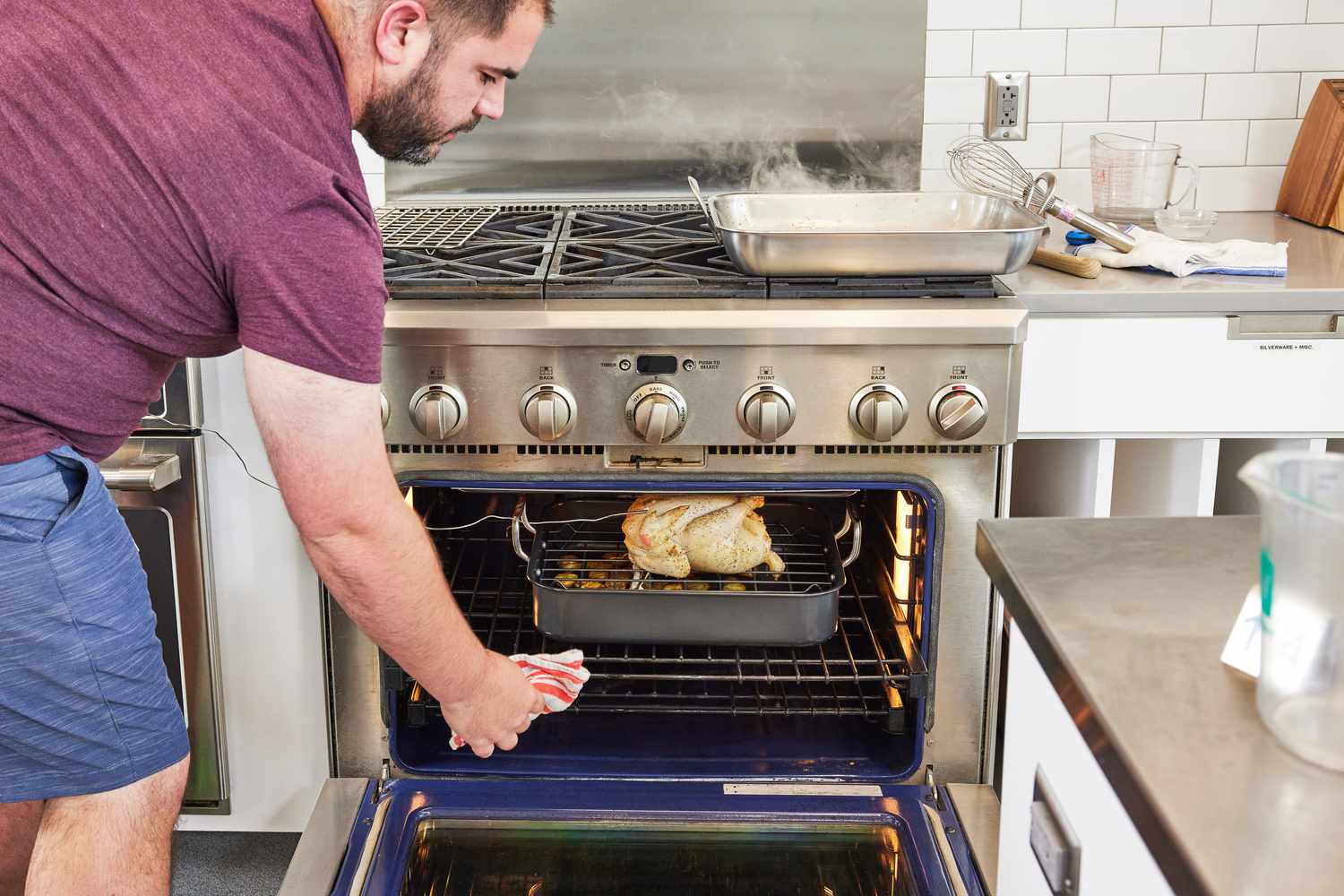 Person putting the Rachael Ray 16" x 13" Roaster with Dual-Height Rack with chicken and potatoes into the oven