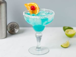 Blue margarita on the rocks with salt along with an orange and cherry garnish