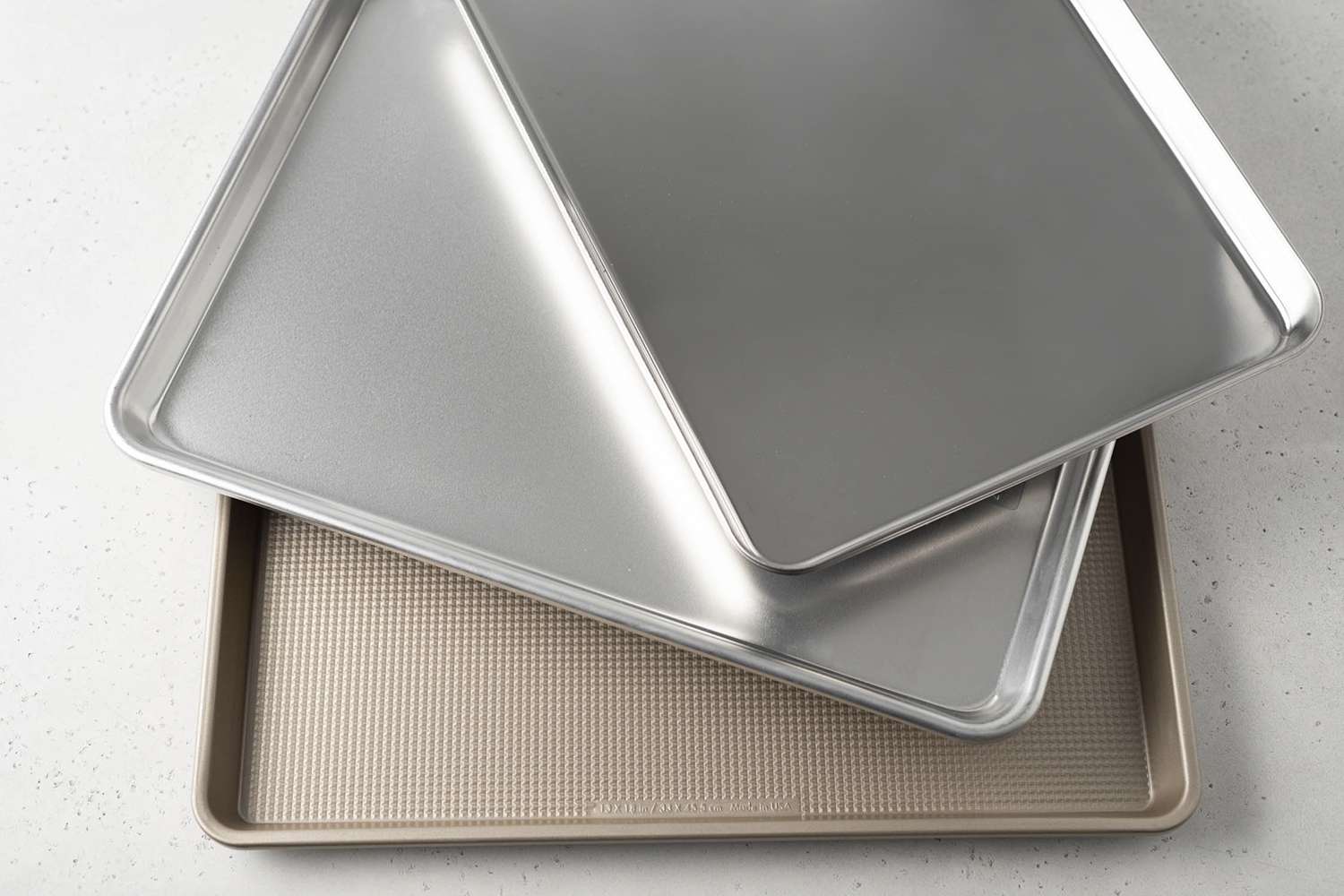 Assortment of baking sheets we recommend layered on top of each other displayed on a white surface