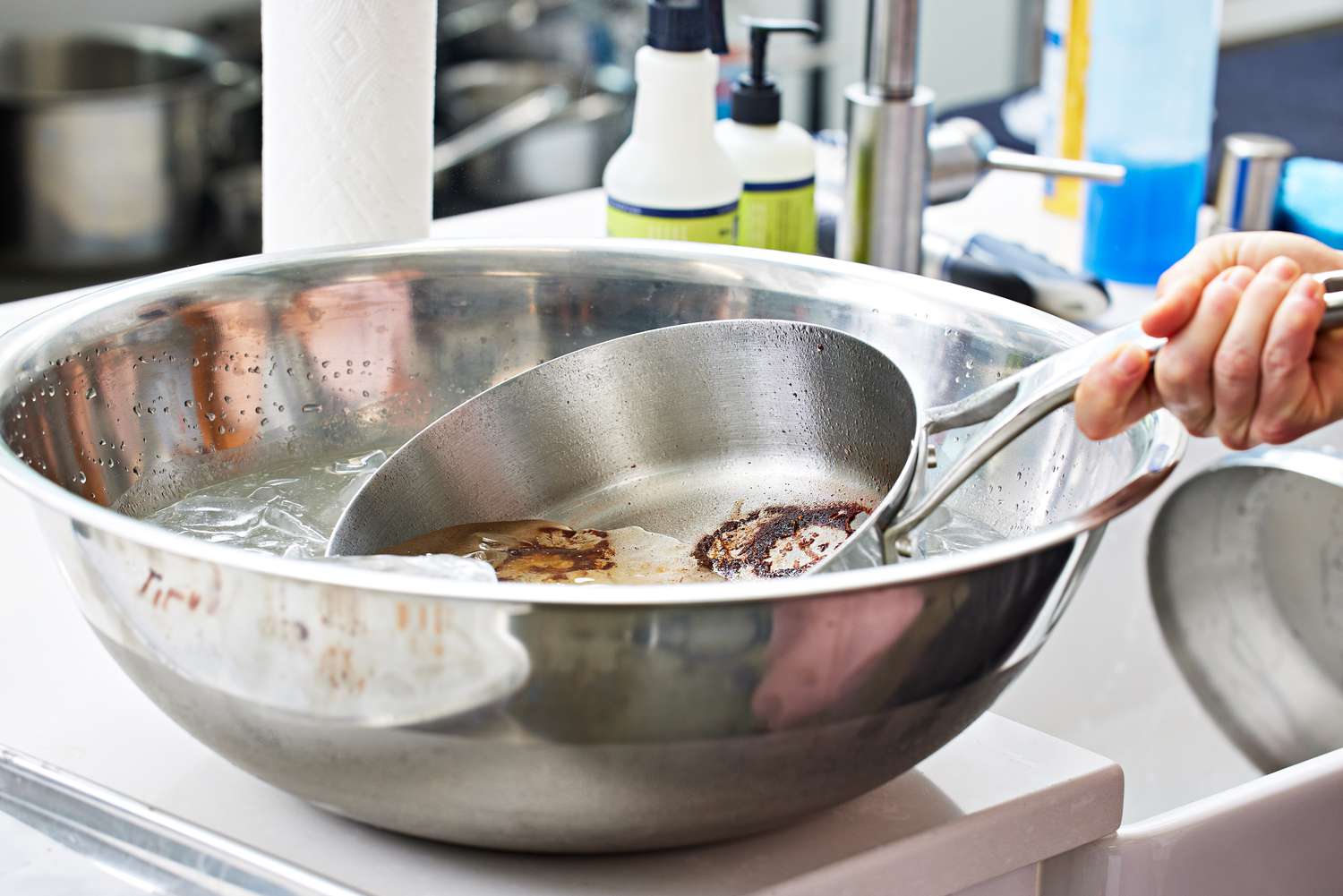 Person dunking a dirty pan from the Anolon Nouvelle Stainless 10-Piece Cookware Set into a bowl of ice water