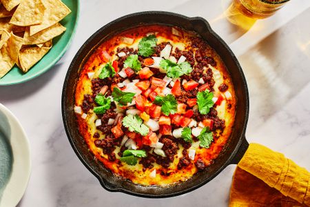 A cast iron skillet with choriqueso topped with diced onions, tomatoes, and cilantro, and served with pita chips