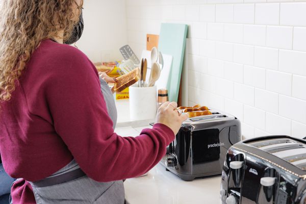 Person standing next to the Proctor Silex 4-Slice Wide Slot Toaster and another toaster on a kitchen counter 