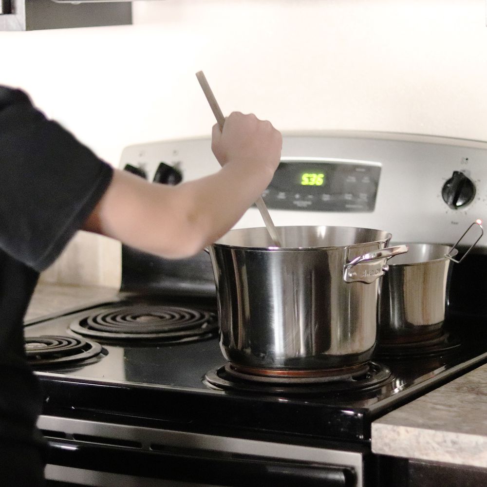 Person stirring a pot from the Anolon Nouvelle Copper Stainless Steel 10-Piece Cookware Set on a stove
