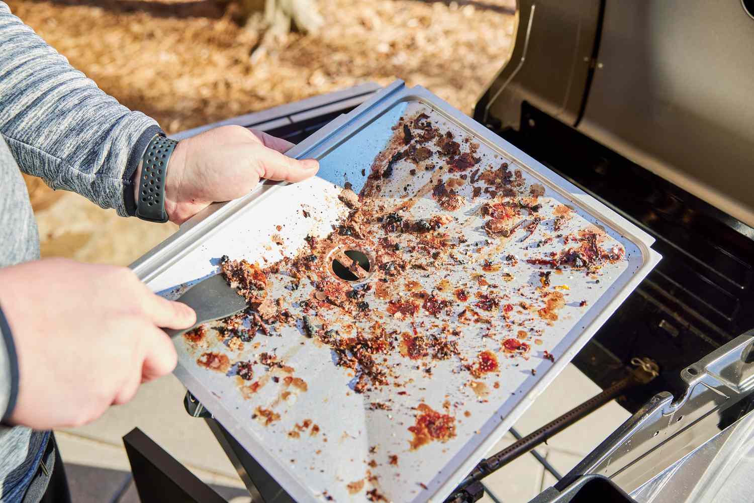 Person scraping food off the drip tray of the Char-Broil 463630021 Performance Series 2-Burner Gas Grill