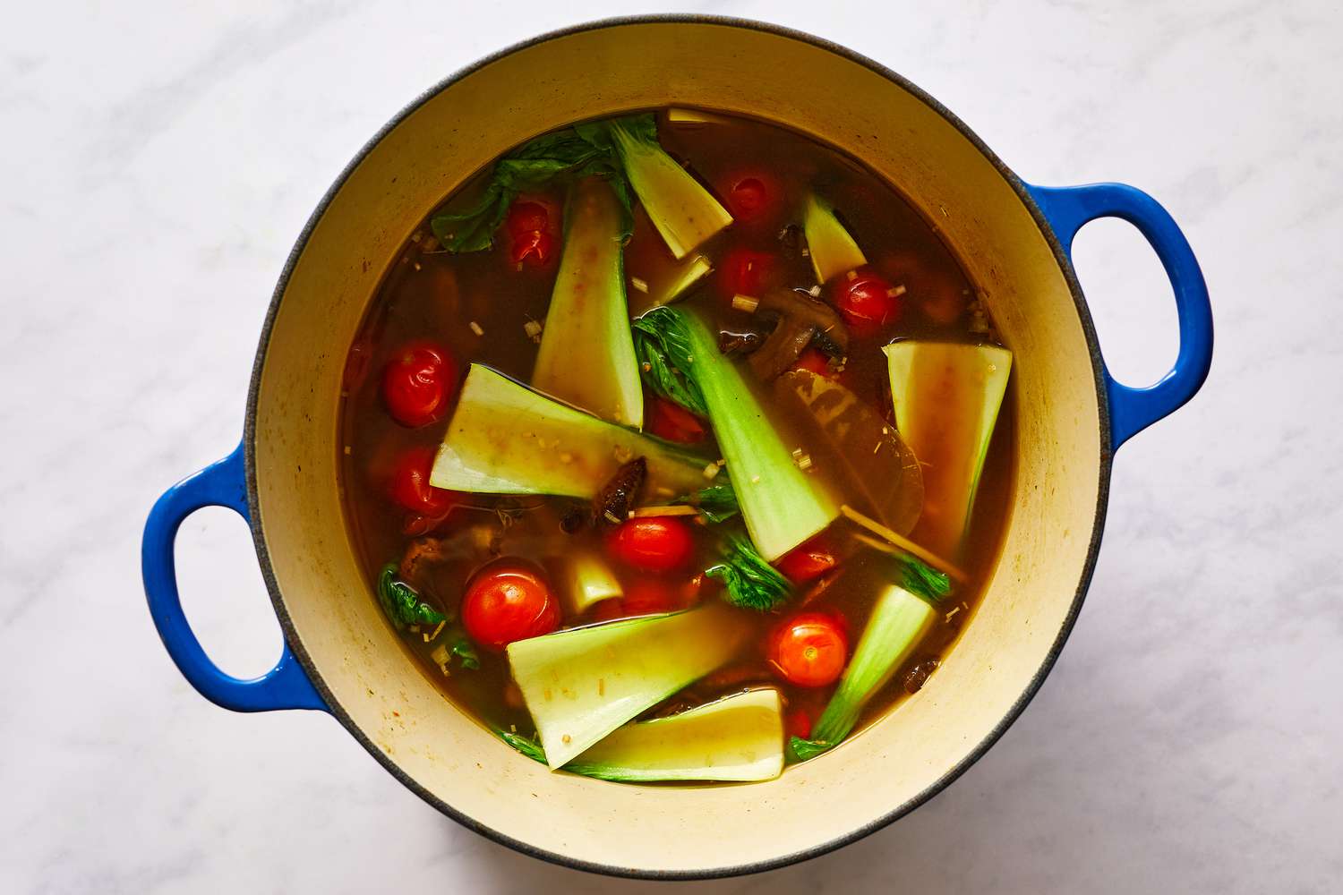 Bok choy and cherry tomatoes added to the soup in the pot 