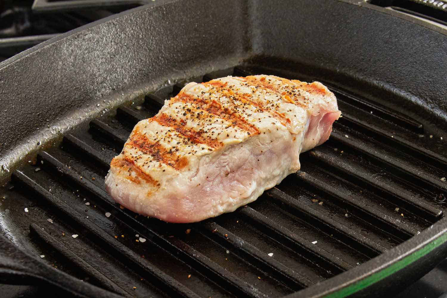 Close-up of a pork chop being grilled on the Lodge Seasoned Cast Iron Square Grill Pan showing grill marks.