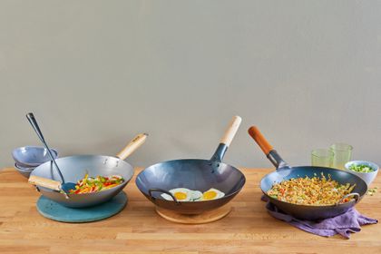 Three woks on a wooden table, holding stir-fry, fried eggs, and fried rice