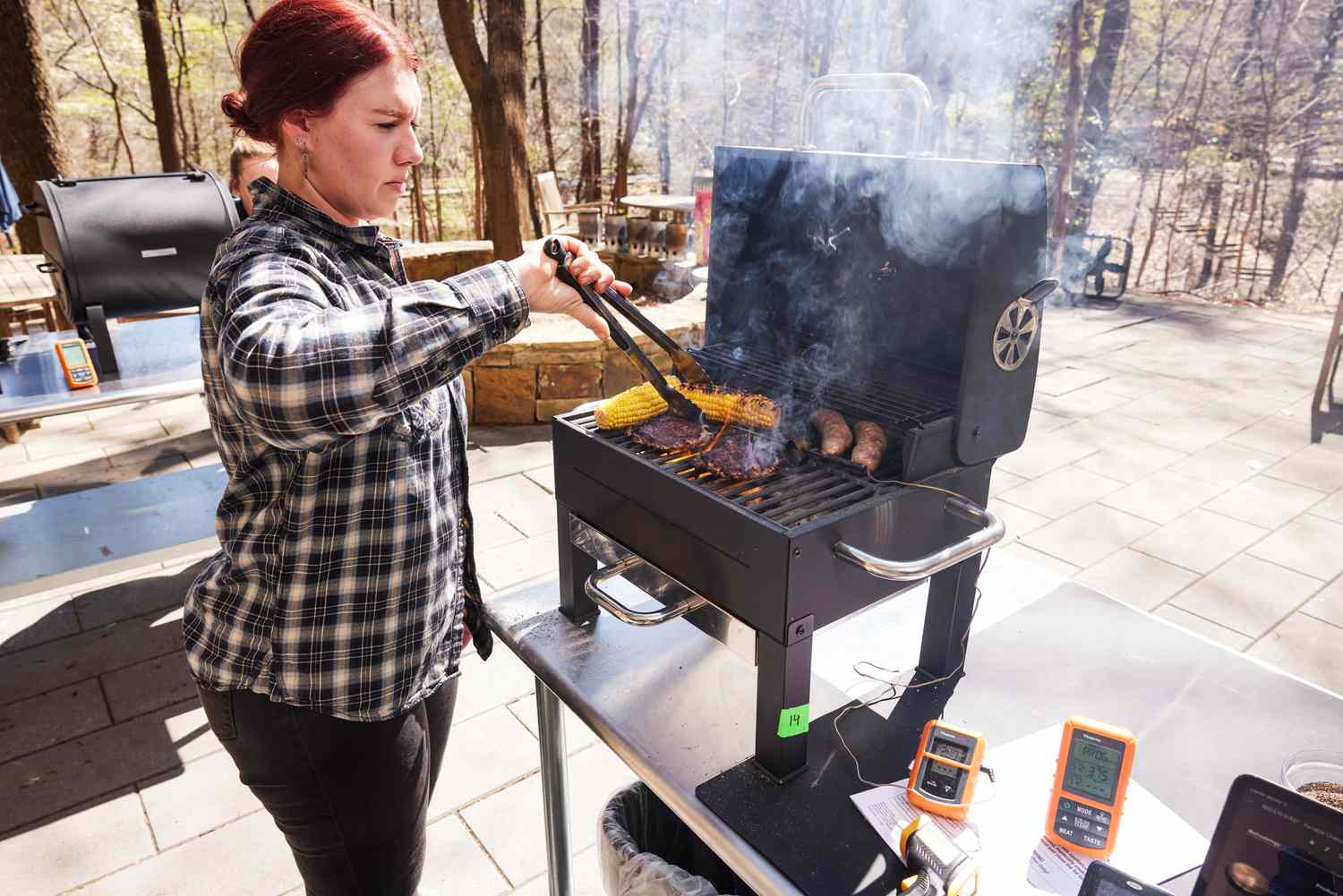 Woman flipping corn cooking on the Expert Grill Premium with burgers and sausages outside 