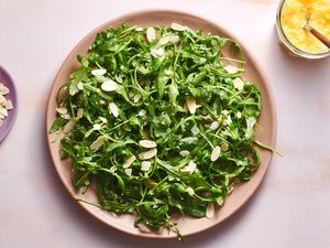 A large plate of arugula salad with whole lemon vinaigrette, topped with sliced almonds