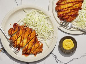 Two plates of pork tonkatsu served with shredded cabbage and spicy mustard