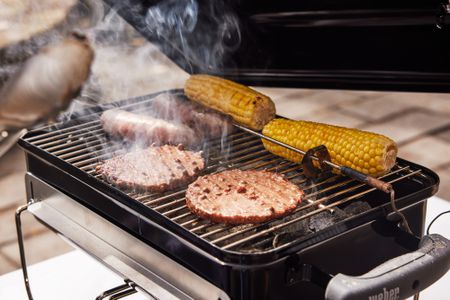 Burger patties, sausages and corn cooking on a Weber Go-Anywhere Charcoal Grill