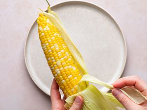 hands peeling husk off of microwaved corn cob