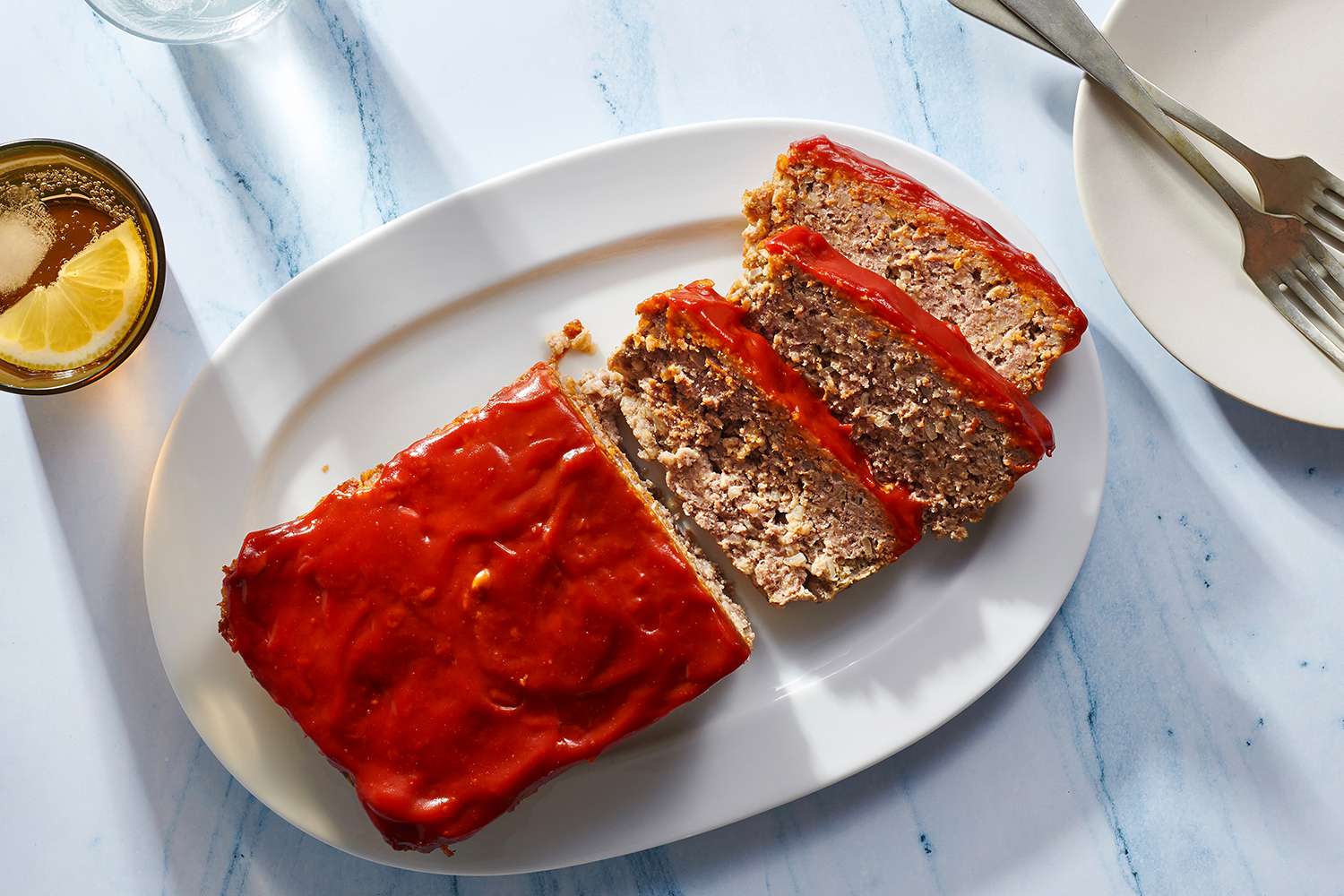 Partially sliced meatloaf with oatmeal topped with ketchup glaze on white serving platter