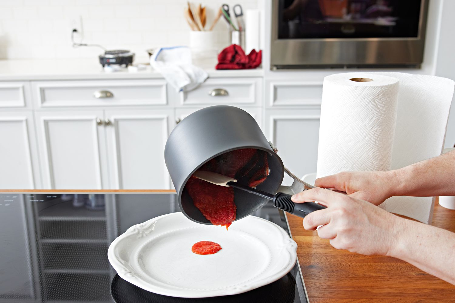 Person scraping sauce from a pot in the Calphalon Signature Nonstick 10-Piece Cookware Set onto a plate