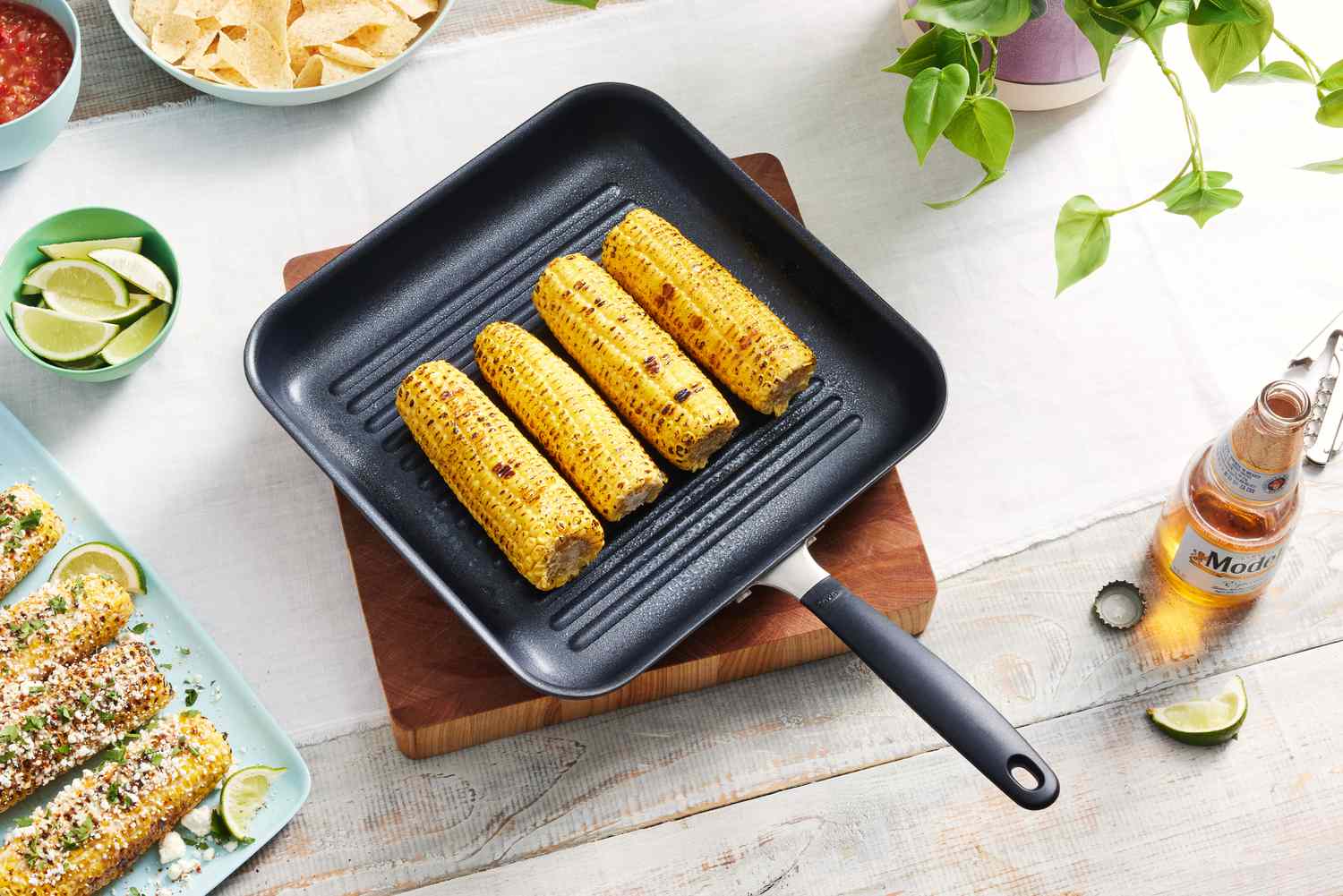 The OXO Good Grips 11” Square Grill Pan on a table with grilled corn in the pan and other food on the table. 